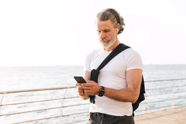 Image of thinking old man using earpod and cellphone while working out — Stock Photo, Image