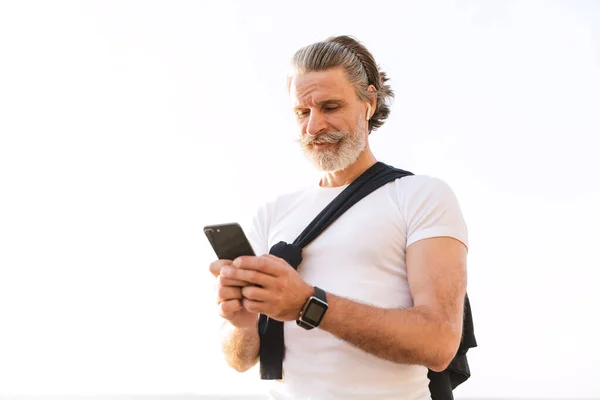 快乐的老人一边锻炼一边用耳机和手机的画面 — 图库照片