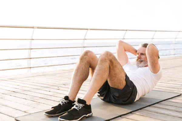 Image of strong old man doing exercise on mat while working out