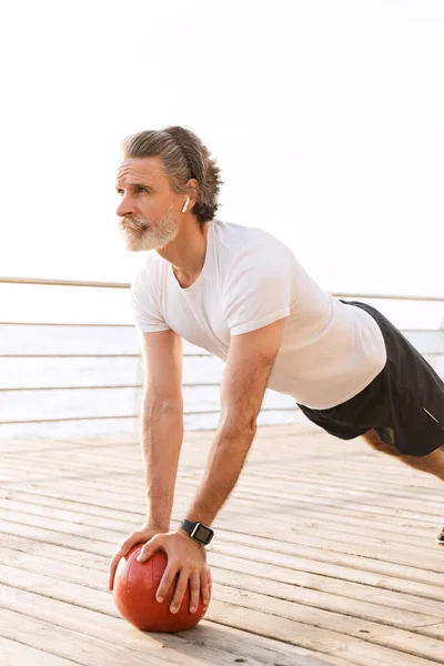 Image of bearded old man doing exercise with medicine ball