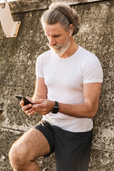 Obraz białego starszego mężczyzny korzystającego ze słuchawki i telefonu komórkowego — Zdjęcie stockowe