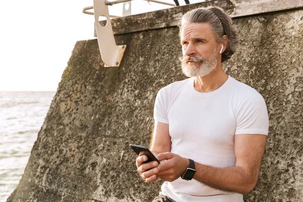 Obrázek bělocha staršího muže používajícího sluchátka a mobil — Stock fotografie
