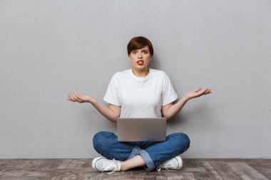 Image of uptight woman sitting on floor and using laptop compute