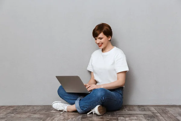 Зображення радісної жінки, що сидить на підлозі і використовує ноутбук — стокове фото
