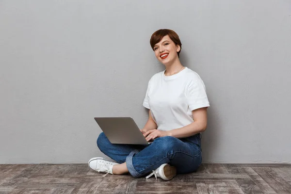 Image of happy woman sitting on floor and using laptop computer — Stockfoto