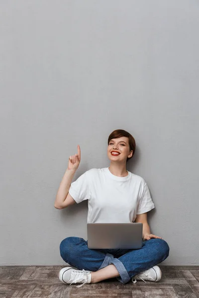 Immagine di giovane donna che punta il dito verso l'alto mentre si siede con l — Foto Stock
