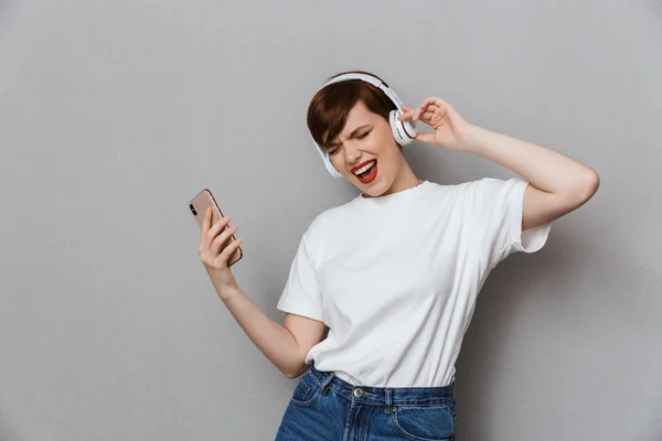 Εικόνα εκπληκτικής νεαρής γυναίκας που τραγουδάει με ακουστικά και smartpho — Φωτογραφία Αρχείου