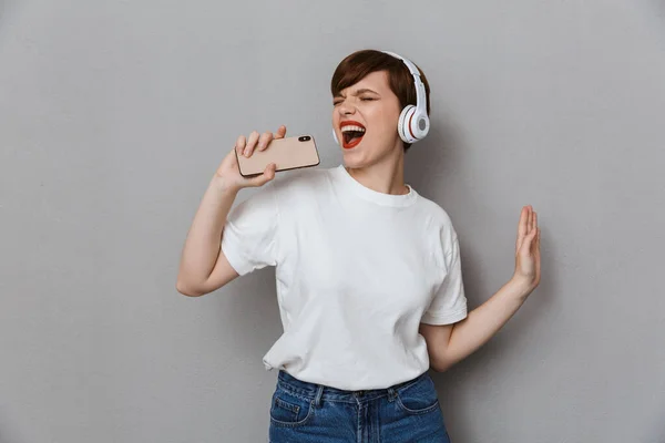 Imagen de una joven feliz cantando con audífonos e smartphon —  Fotos de Stock