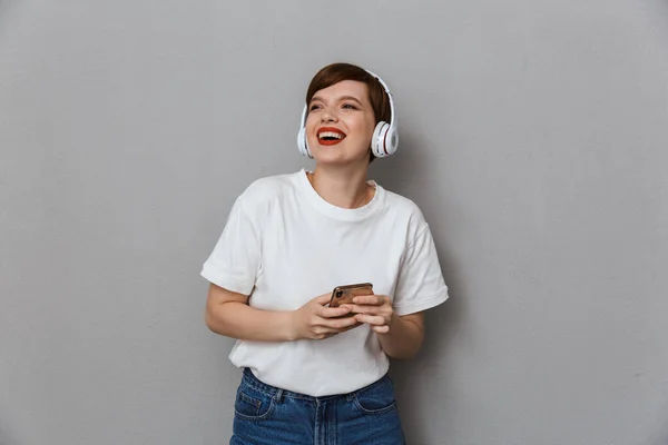 Imagen de una mujer joven con auriculares sonriendo y sosteniendo la celda —  Fotos de Stock