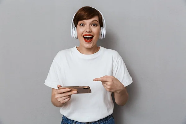 Imagen de una mujer joven usando auriculares jugando juegos en cellpho —  Fotos de Stock