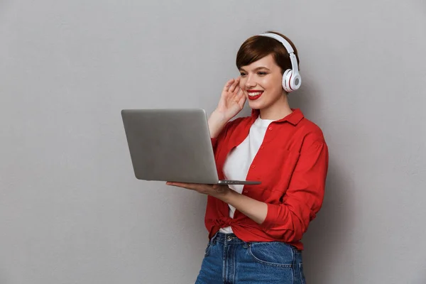 Image of young woman in headphones smiling while holding laptop — Stok fotoğraf