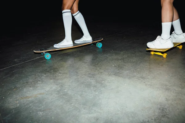 Cropped image of young hipster girls riding skateboards at night — Stock Photo, Image