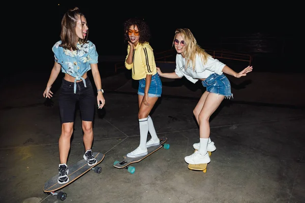 Imagem de meninas multinacionais elegantes andando de skate à noite — Fotografia de Stock