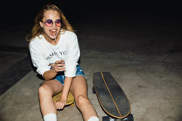 Imagem da menina loira comendo pirulito e andar de skate no nig — Fotografia de Stock