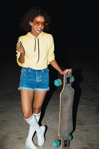 Bild av hipster afrikansk amerikansk flicka som håller skateboard på nig — Stockfoto