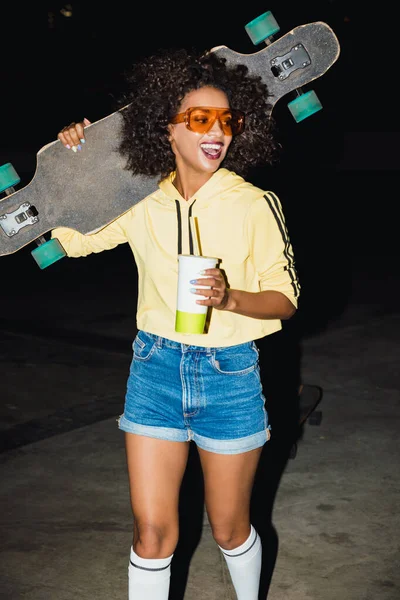 Vrouw 's nachts lopen door straat met skateboard. — Stockfoto