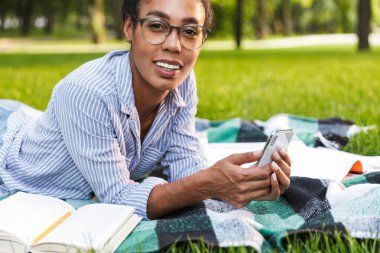 Parkta akıllı telefon tutan mutlu bir Afrikalı Amerikalı kadın.