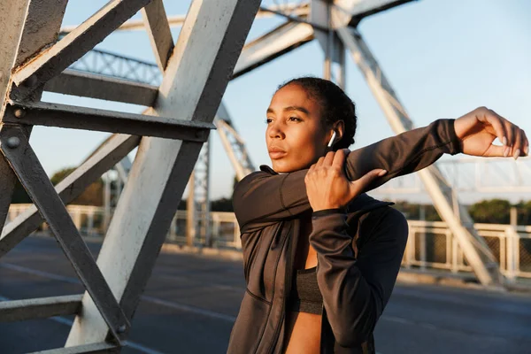 Foto de una mujer afroamericana usando auriculares y estirando los brazos — Foto de Stock