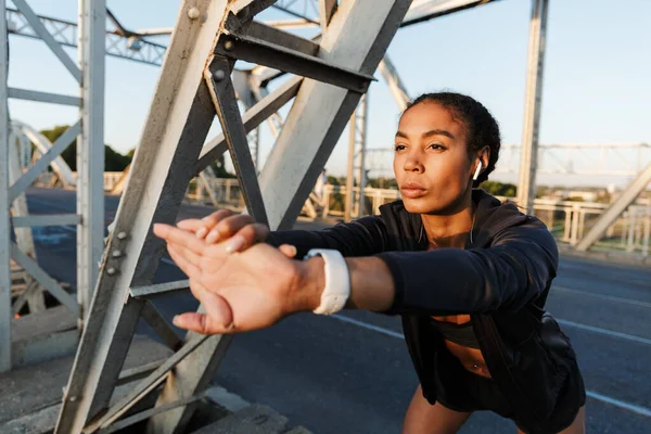 Foto de una mujer afroamericana usando auriculares y estirando los brazos — Foto de Stock