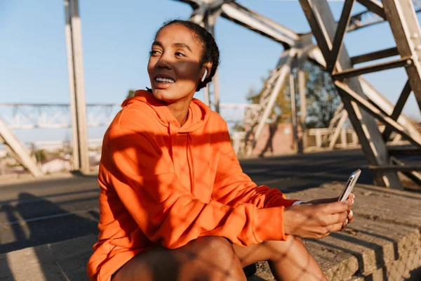 EarPods 와 핸드폰을 사용하여 웃고 있는 아프리카 계 미국인 여성의 사진 — 스톡 사진
