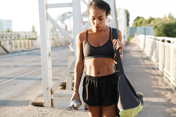 Foto di donna afro-americana che usa gli auricolari mentre cammina con la borsa — Foto Stock