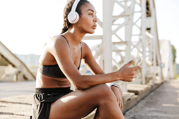 Foto de una joven afroamericana usando auriculares y teléfono celular — Foto de Stock