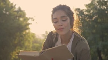 Parkta yatarken gülümseyen ve kitap okuyan güzel, esmer bir kadın.