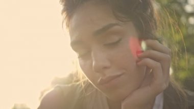 Parkta uzanırken gülümseyen ve neşeli hisseden büyüleyici, cilveli, genç esmer kadının yakın görüntüsü.