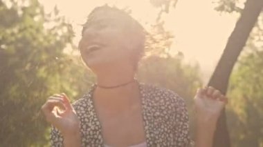 Neşeli genç esmer kadın ıslak saçlarını sallıyor ve parkta eğlenirken yüzünü buruşturuyor.