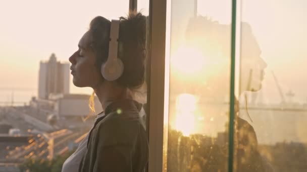在阳台上一边听音乐一边拍照 一边用智能手机聊天的快乐的年轻黑发女人的侧影 — 图库视频影像