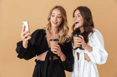 Kahve içerken cep telefonu kullanan iki mutlu kadının portresi.
