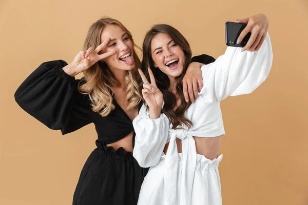Ritratto di due donne divertenti che usano lo smartphone mentre gesticolano il segno della pace — Foto Stock