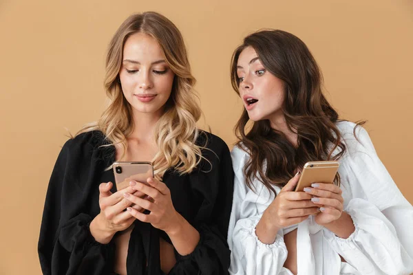 Portré két kíváncsi gyönyörű nő nézi okostelefonok — Stock Fotó