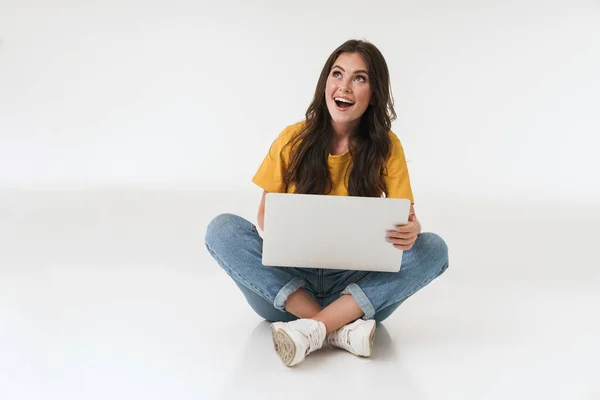 Emocjonalnie zaskoczona młoda kobieta odizolowana na białym tle ściany za pomocą laptopa. — Zdjęcie stockowe