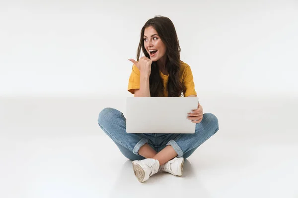 Surpreendida jovem mulher isolada sobre fundo da parede branca usando computador portátil apontando . — Fotografia de Stock
