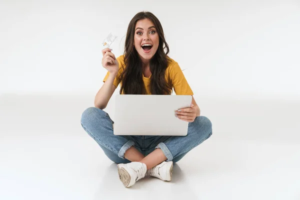 İyimser bir bakış açısıyla genç bir kadın, elinde kredi kartı olan dizüstü bilgisayarla beyaz duvar arkasından izole edilmiş.. — Stok fotoğraf