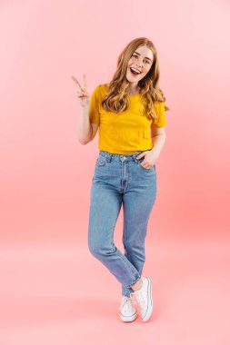 Mutlu neşeli iyimser kız pembe duvar arkasında izole edilmiş barış jesti gösteriyor..