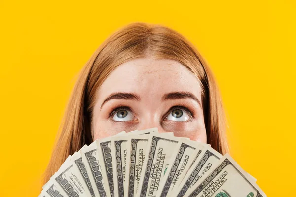 Chica aislada sobre fondo de pared amarilla cubriendo la cara con dinero mirando a un lado . —  Fotos de Stock