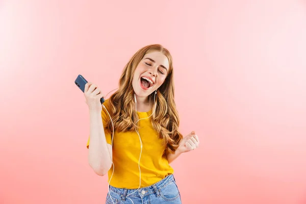 Emocionální dívka izolované přes růžové stěny pozadí pomocí mobilního telefonu poslech hudby se sluchátky. — Stock fotografie