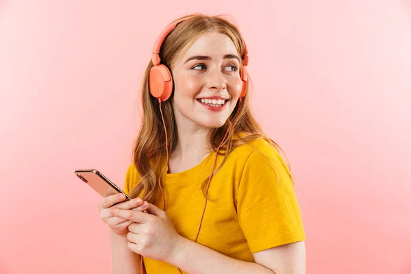 Fille isolée sur fond de mur rose en utilisant le téléphone mobile écouter de la musique avec des écouteurs . — Photo