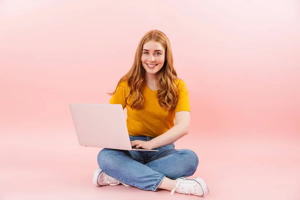 Chica alegre sonriente positiva aislado sobre fondo de pared rosa utilizando ordenador portátil . — Foto de Stock