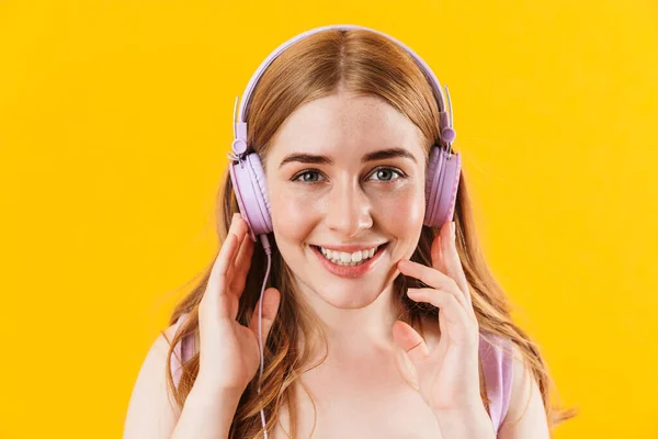 Chica feliz aislado sobre fondo amarillo de la pared escuchando música con auriculares . — Foto de Stock