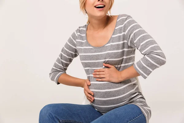 Imagen recortada de la mujer embarazada feliz tocando su vientre mientras está sentada —  Fotos de Stock