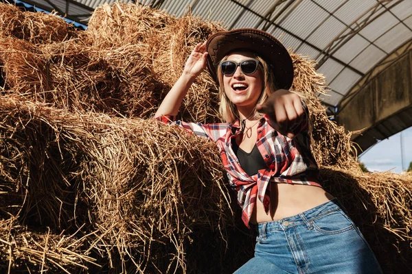 Bela jovem loira vaqueira de pé no celeiro — Fotografia de Stock