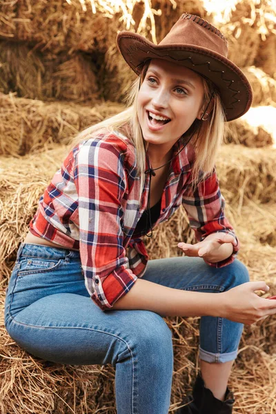 美丽而快乐的金发女牛仔坐在谷仓前 — 图库照片