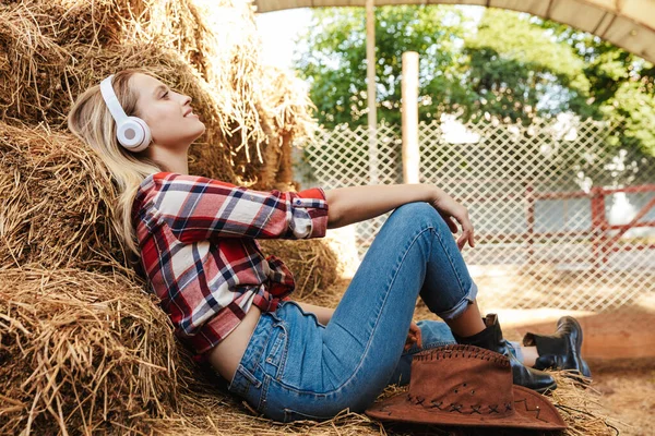 Sorridente giovane cowgirl bionda seduta su un pagliaio al fienile — Foto Stock