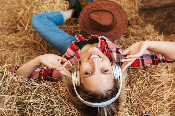 年轻的金发女牛仔坐在谷仓的草堆上笑着 — 图库照片