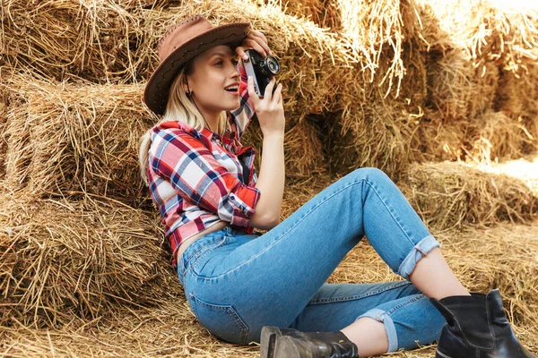 Glimlachen jong blond cowgirl ontspannen op een hooiberg — Stockfoto