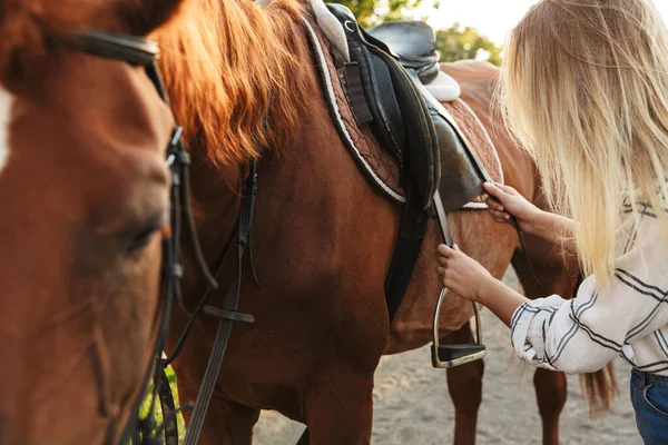 Piękna uśmiechnięta młoda blondynka pieszcząca konia w stajni — Zdjęcie stockowe