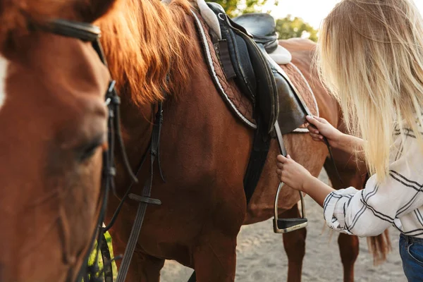 Bela sorridente jovem loira acariciando um cavalo no estábulo — Fotografia de Stock